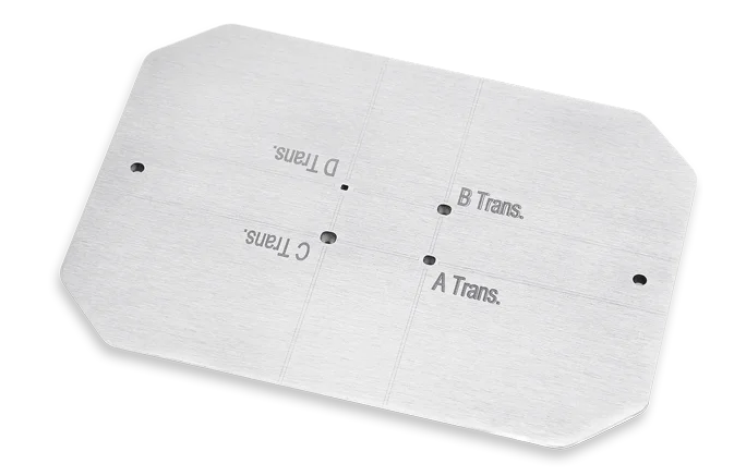Ein rechteckiger Kolimator aus Wolfram-Schwermetall (WSM) mit abgerundeten Ecken, vier kleinen Löchern und eingravierter Bezeichnungen A Trans., B Trans., C Trans. und D Trans.