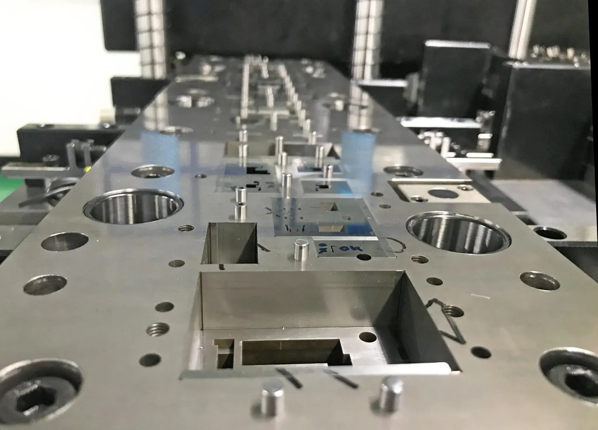 Nahaufnahme einer präzisionsgefertigten Metallkomponente mit verschiedenen Löchern, Schlitzen und Stiften, wahrscheinlich Teil einer industriellen Form oder eines Werkzeugs für Fertigungsprozesse.
